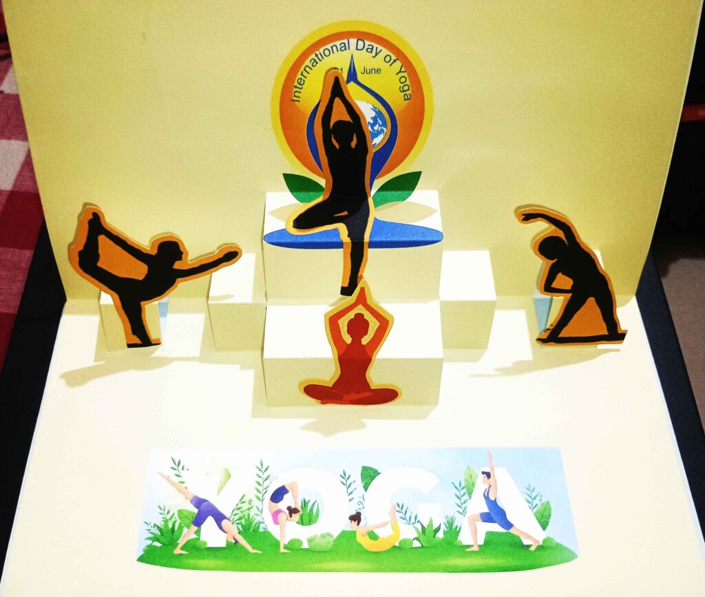 Opened view of the Chennai pop-up cover, featuring layered paper figures performing yoga postures beneath the International Day of Yoga emblem.